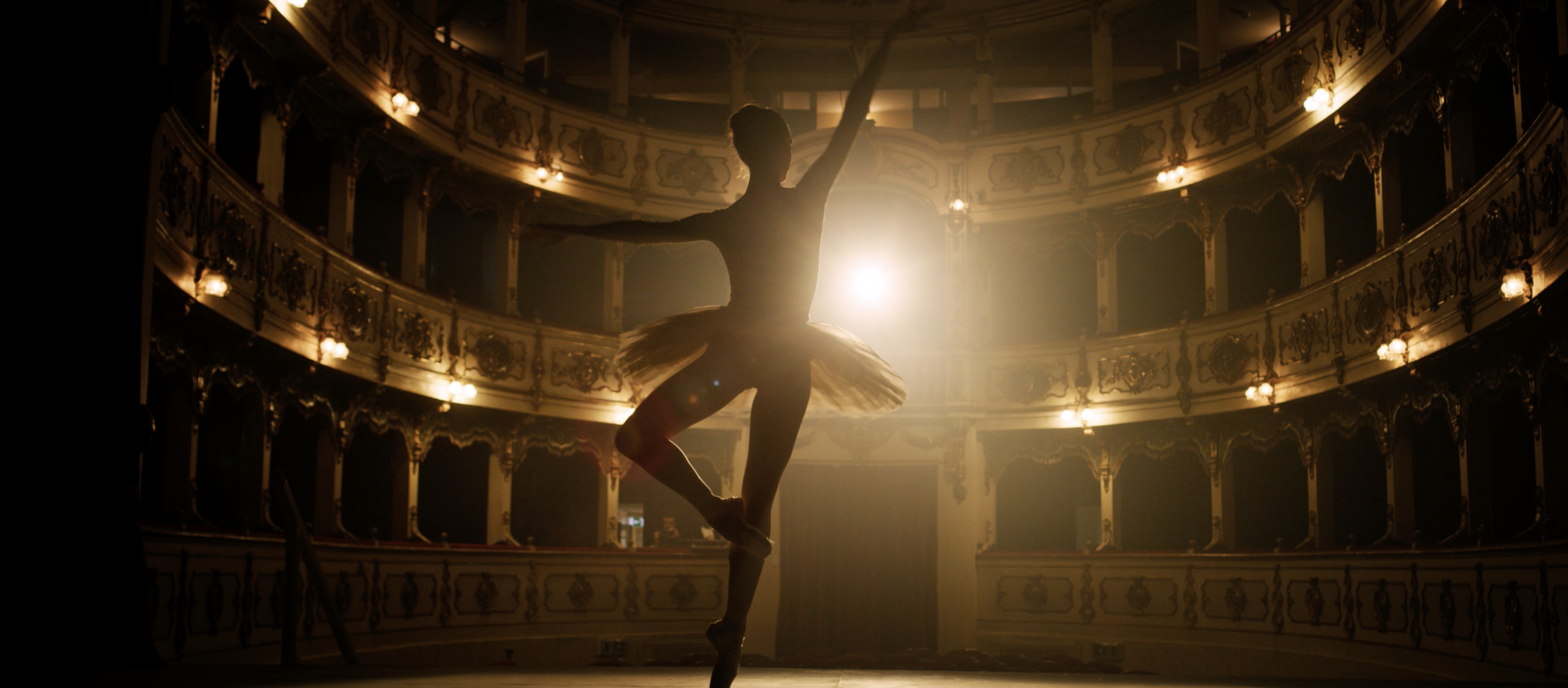 Ballet dancer performing on stage inside an ornate historic theatre with cinematic backlighting.
