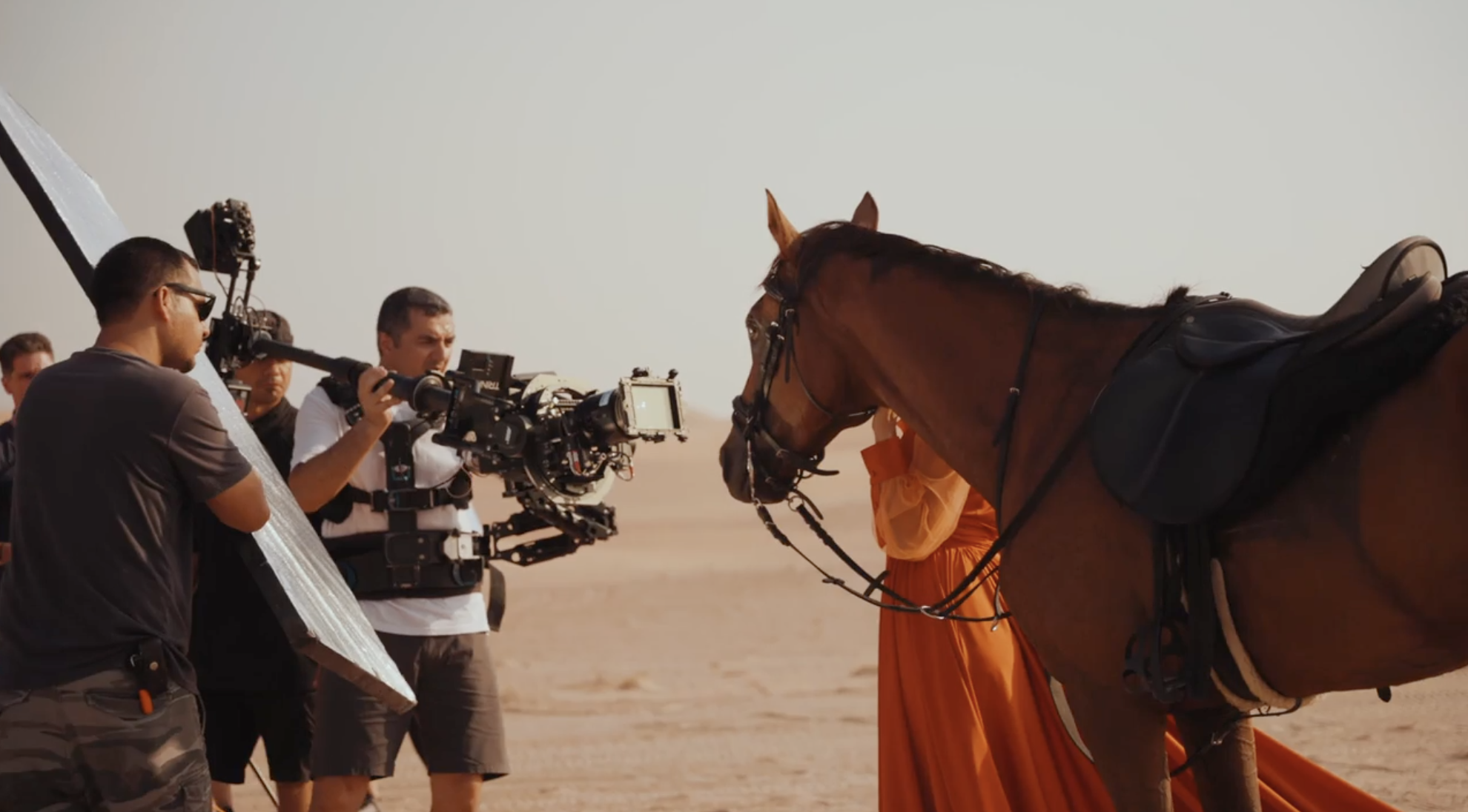 Toosuns film crew shooting a cinematic desert campaign with a model in an orange dress and a horse.
