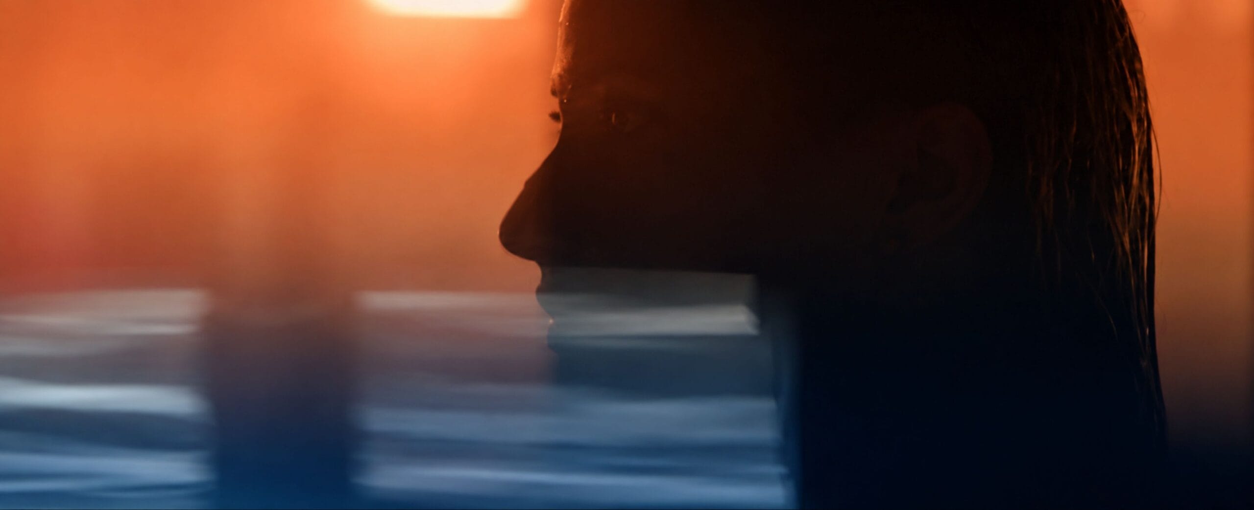 Woman's silhouette at sunset with warm orange light and blurred water