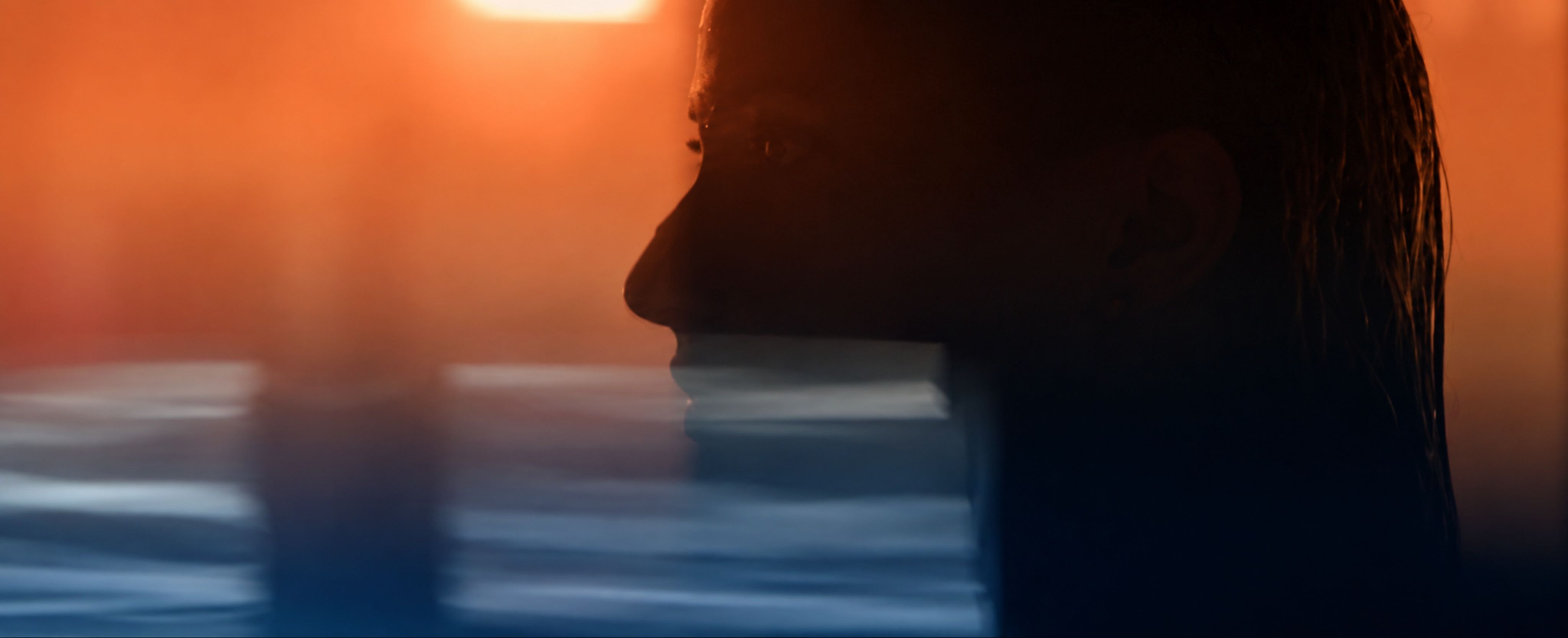 Woman's silhouette at sunset with warm orange light and blurred water