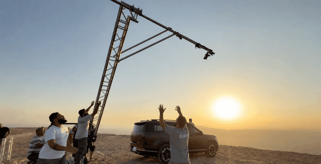 Behind the scenes of a Hyundai automotive campaign, with a camera crane filming an SUV at sunset in the desert