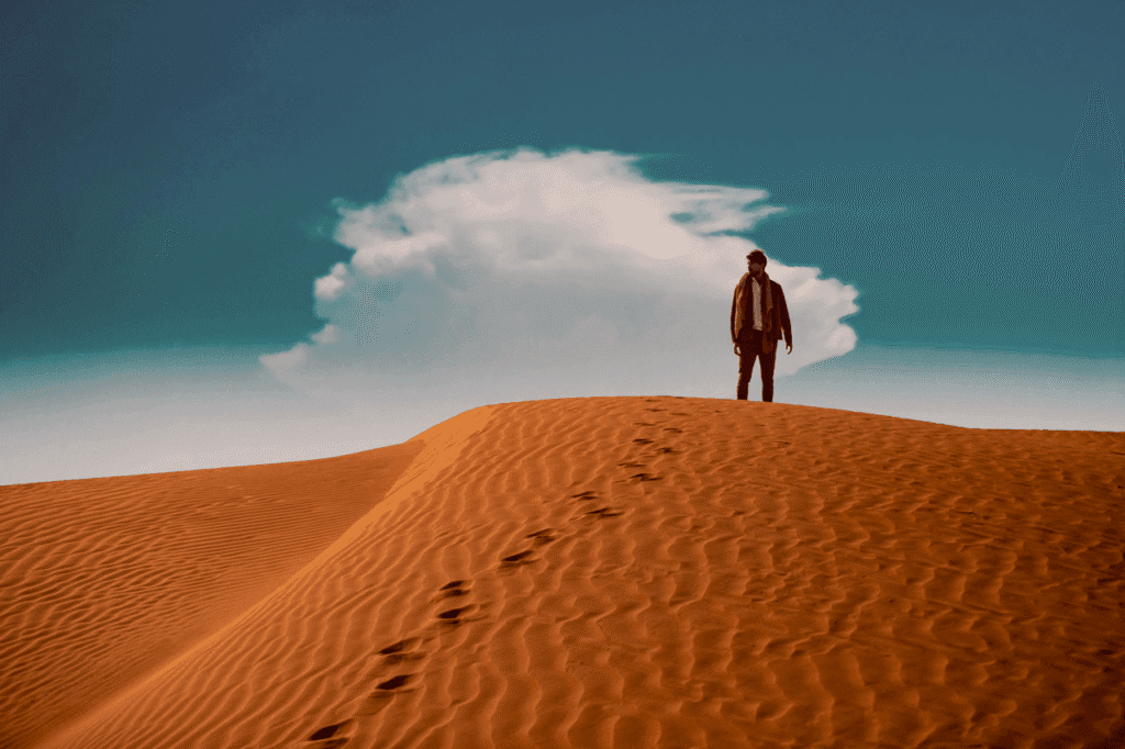 Man standing on a desert dune beneath a dramatic cloud in the Six Senses Residences campaign film.