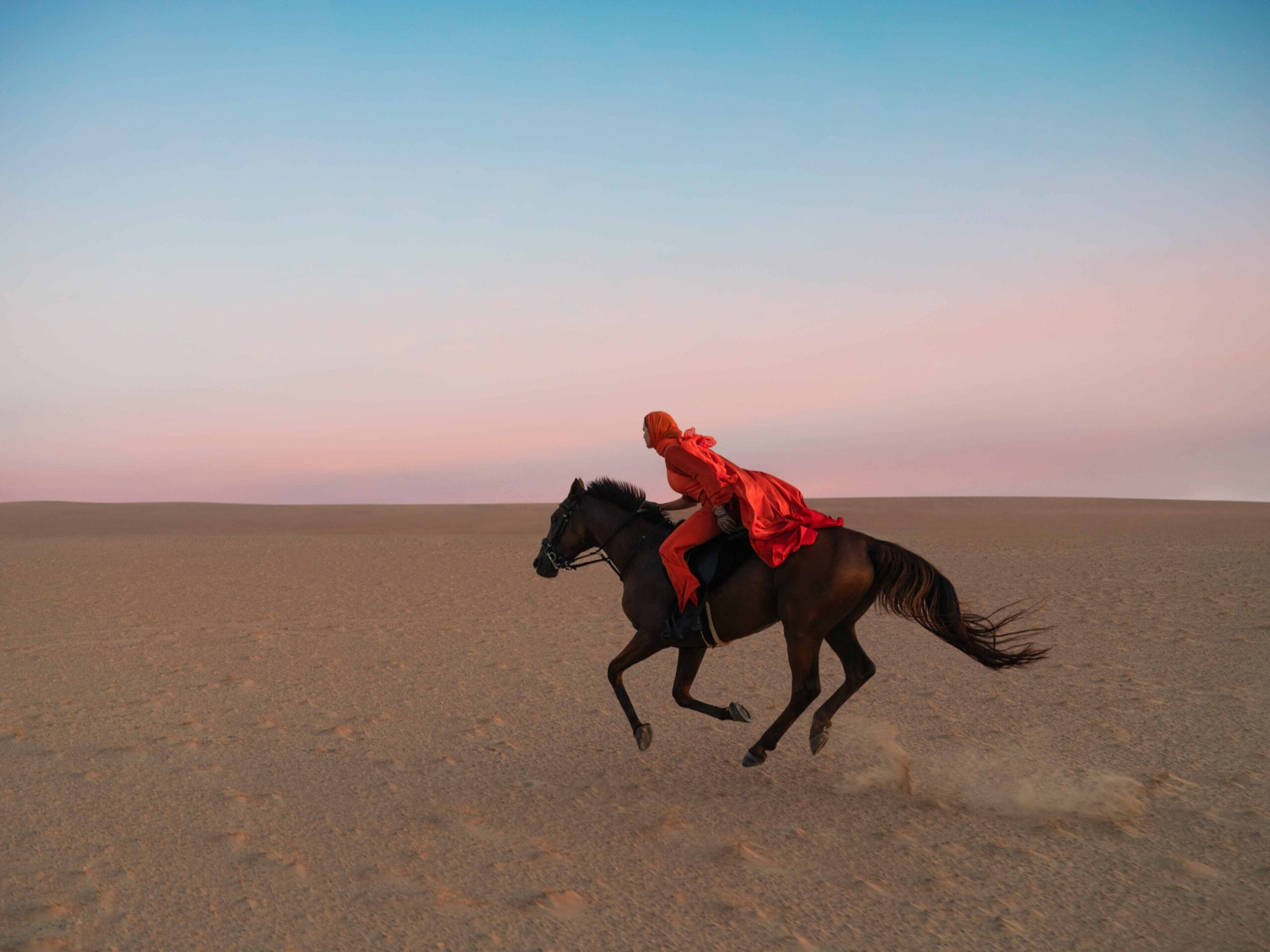 Horse and rider in red riding across dubai desert dunes