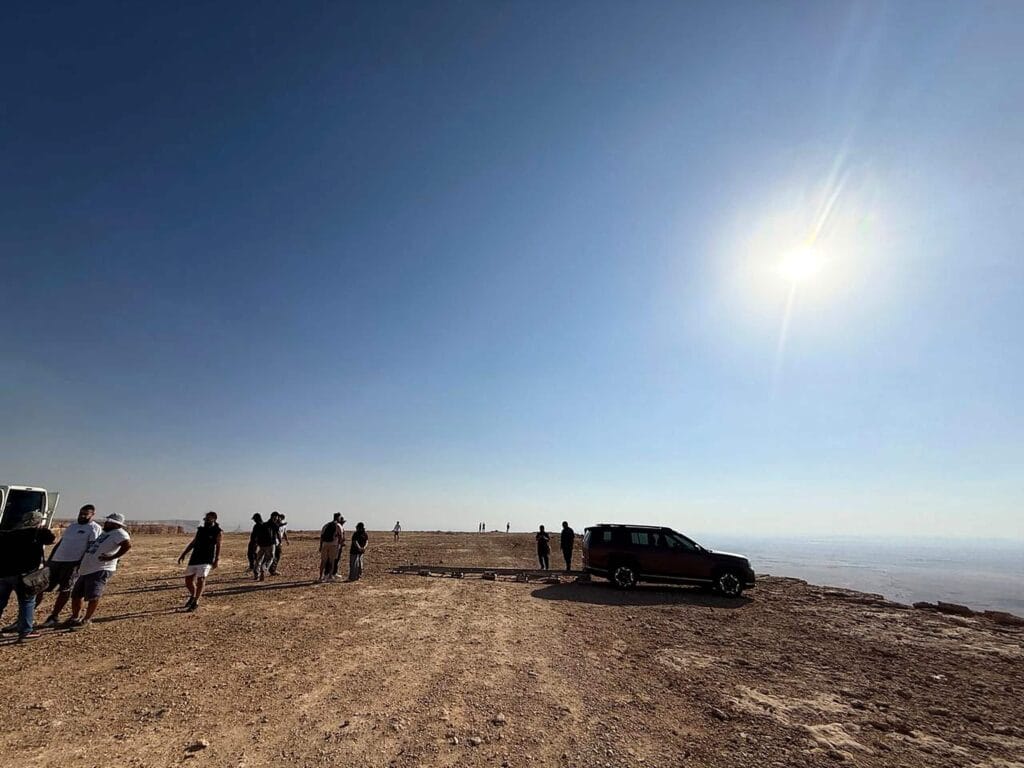 Film crew scouting a desert location beside a parked production vehicle under a bright blue sky