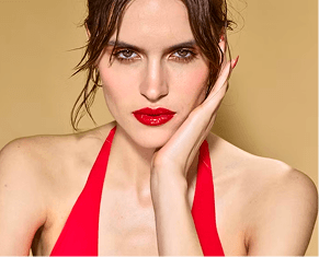 Woman in a red halter top with bold red lipstick posing against a beige background