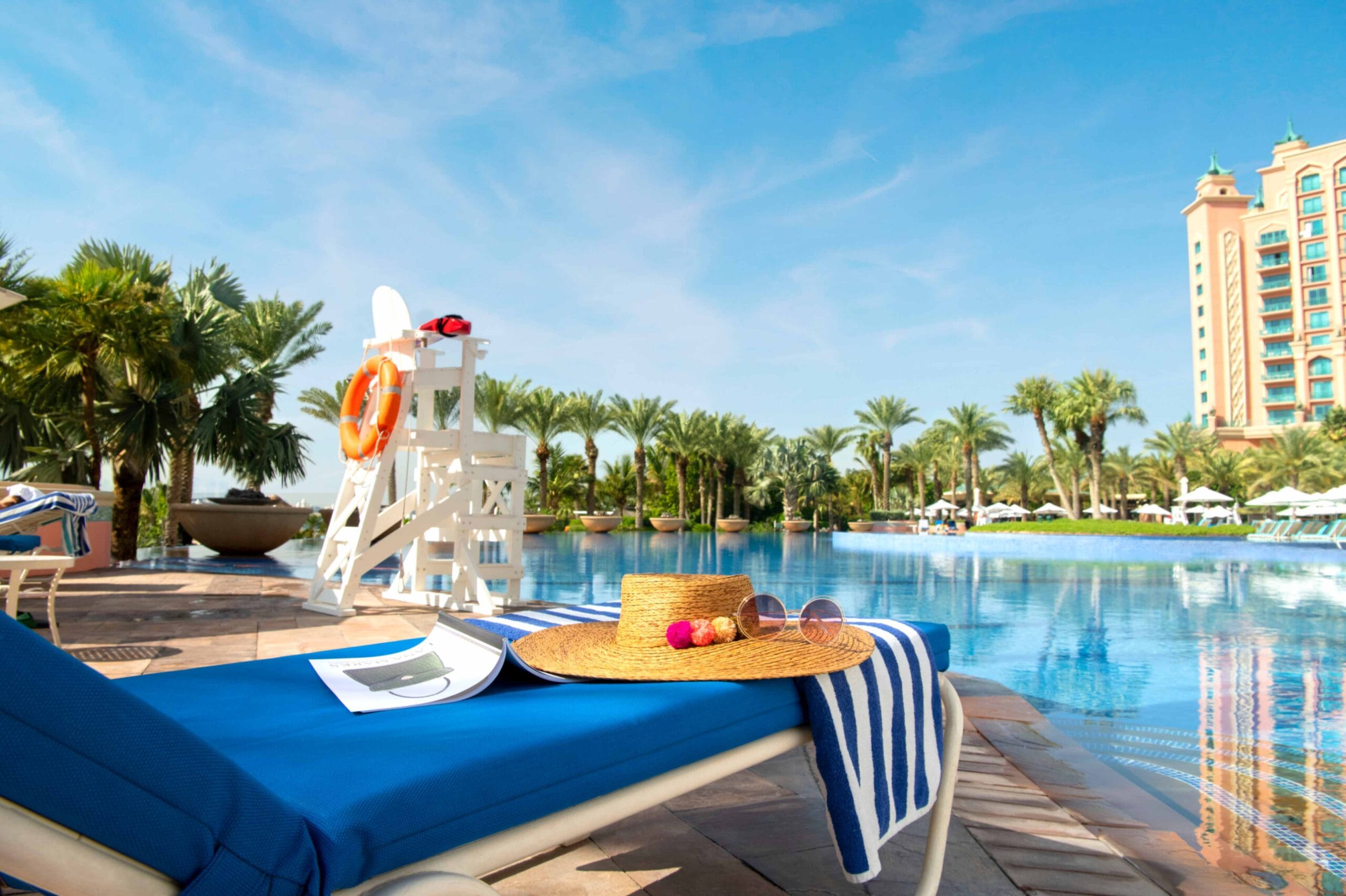 Atlantis Aquaventure resort pool in Dubai with a sun lounger, hat and palm trees.