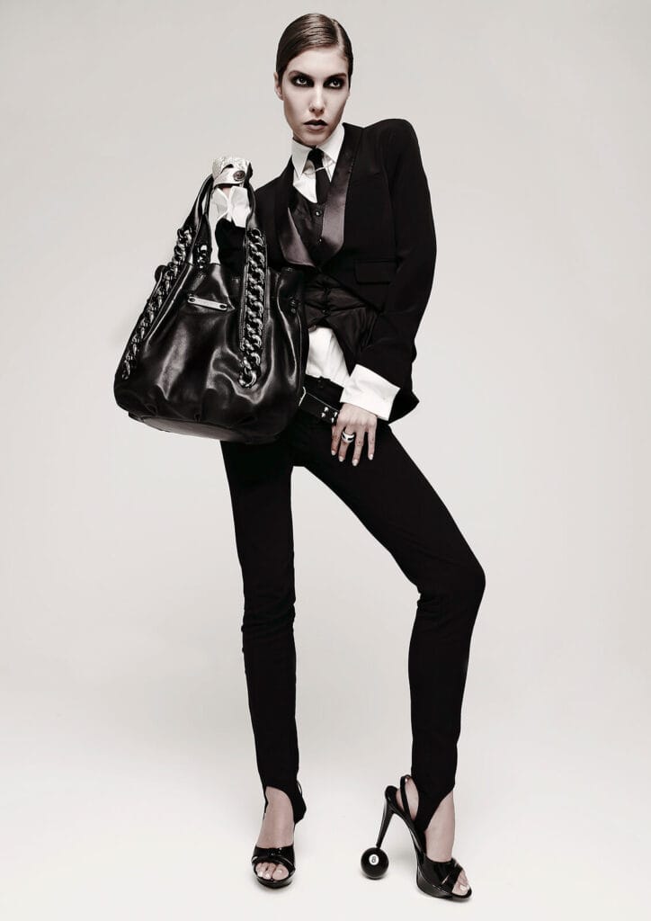 Luxury fashion editorial featuring a model in a black tailored suit with an oversized leather handbag.