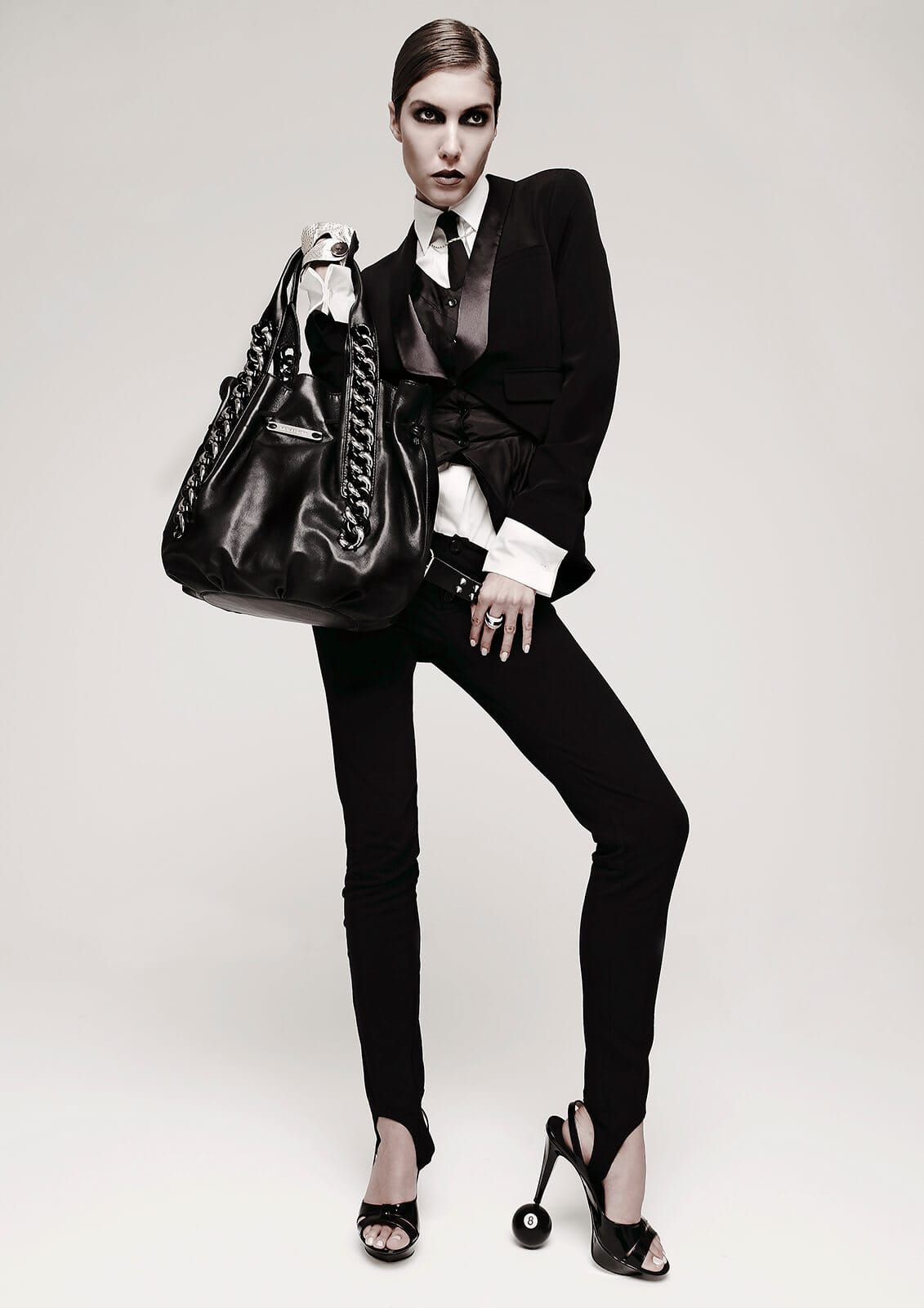 Luxury fashion editorial featuring a model in a black tailored suit with an oversized leather handbag.