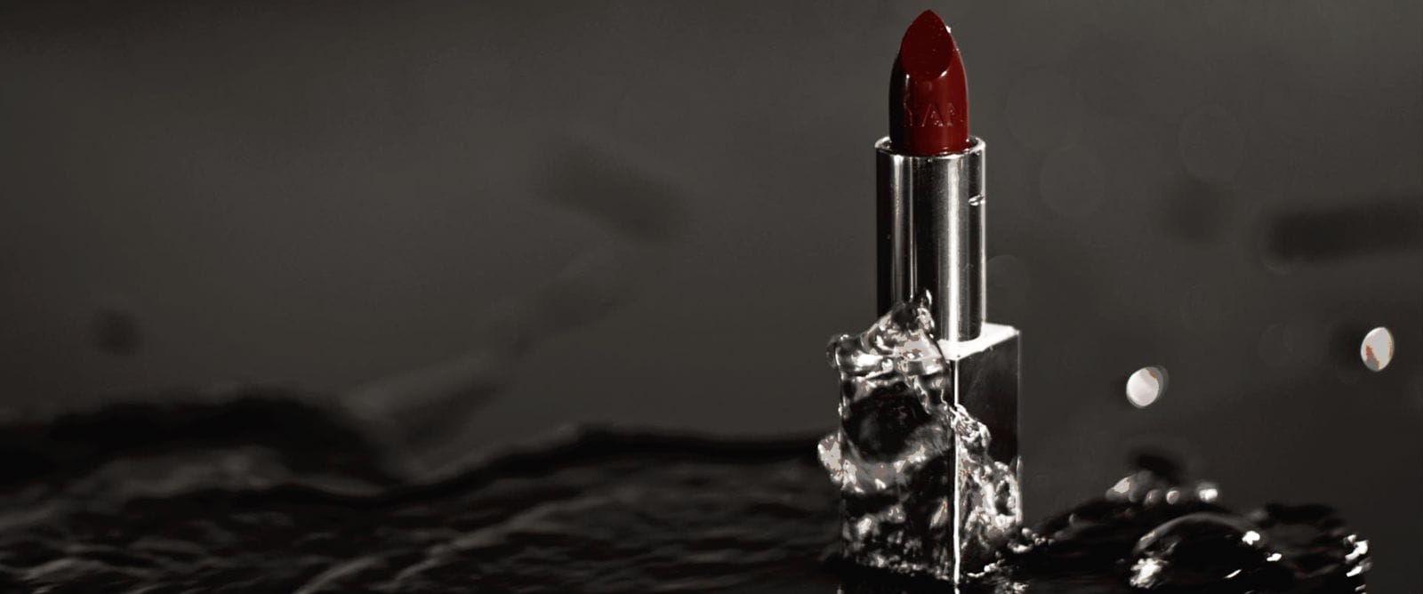 Ayan Beauty red lipstick emerging from black water in a cinematic product shot