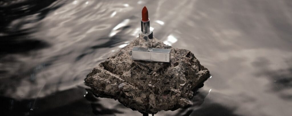 Ayan Beauty lipstick displayed on a textured rock surrounded by reflective water