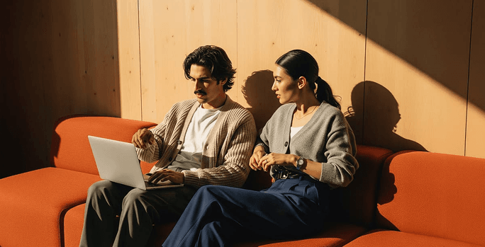 Two creative professionals collaborating on a laptop in a sunlit contemporary workspace.