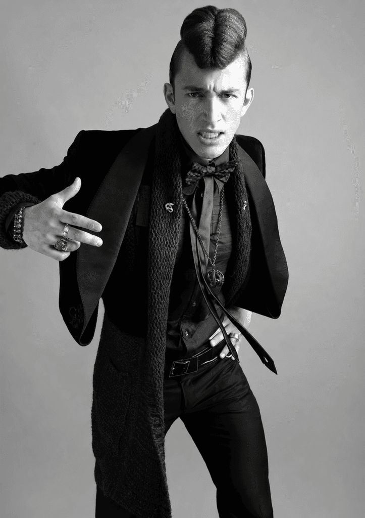 Black-and-white menswear fashion editorial by Toosuns featuring a male model in tailored clothing and statement accessories.